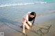 A woman in a pink bikini writing in the sand on the beach.