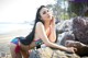 A woman in a bikini sitting on a rock on the beach.