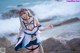 A woman in a sailor outfit standing on a rock by the ocean.