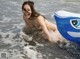 A naked woman is playing in the water with an inflatable raft.