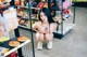 A woman sitting on the floor in front of a shelf of food.